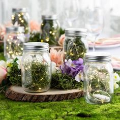 jars filled with plants and flowers on top of a green tablecloth covered in moss