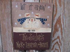 a sign on the side of a wooden fence that says let it snow and two snowmen