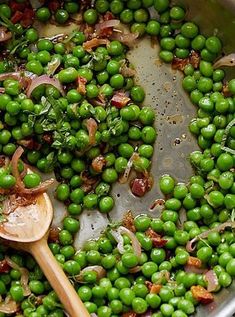 peas and onions are being cooked in a pot with a wooden spoon on the side