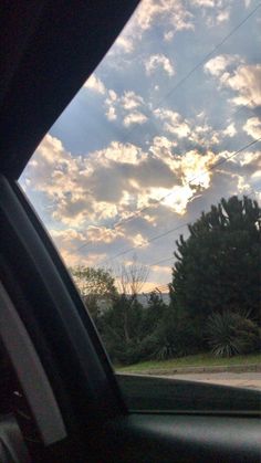 the sun is shining through the clouds in the sky over some trees and bushes, as seen from inside a car window