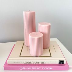 three pink candles sitting on top of a book next to each other in front of a white wall