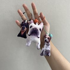 three small dog keychains are being held by someone's hand