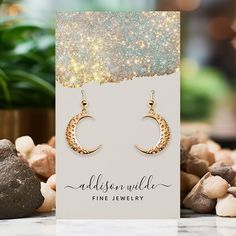 a pair of gold earrings with the words, madison wilde fine jewelry on it next to some rocks