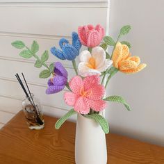 crocheted flowers in a white vase on a table next to an air freshener dispenser