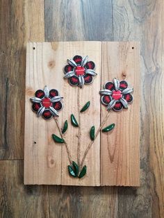 three red and black flowers on wooden planks with green leaves in the center, attached to wood boards