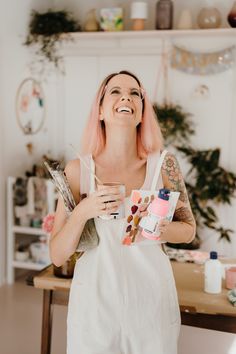 a woman with pink hair is holding a cup and some makeup products in her hands