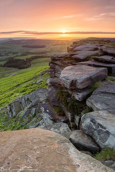 the sun is setting over some rocks on top of a hill with green fields in the background