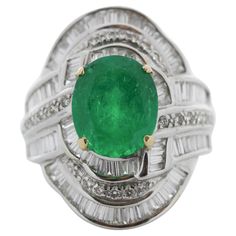 Remarkable in craftsmanship and design, this gorgeous 18k white gold emerald and diamond ring is undeniably unique. An oval cut fine quality emerald sits in the center secured in a prong setting with a weight of 3.89 carats and measures 11.1 X9.3MM. This emerald is complemented by 3.56 carats of shimmering baguette and round brilliant cut diamonds, all channel and prong set in a cascading cluster of brilliance and fire. Platinum Oval Emerald Ring With 17 Jewels, Oval Platinum Emerald Ring With 17 Jewels, Luxury Oval Emerald Ring With Diamond Cut, Exquisite Oval Emerald Ring In Platinum, Timeless Oval Diamond Cut Emerald Ring, Oval Diamond-cut Emerald Ring, Oval Diamond Cut Emerald Ring, Oval Diamond Cut Emerald Ring In Fine Jewelry Style, Exquisite Oval Emerald Ring With Diamond Accents