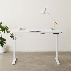 a white desk with a lamp on it next to a potted plant