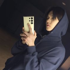 a man in a hoodie holding up a remote control to take a selfie