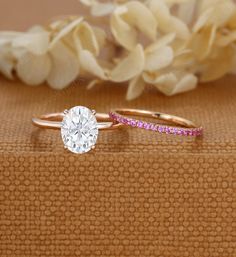 two gold rings with pink and white diamonds on top of each other next to some flowers