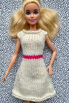 a doll with blonde hair wearing a white knitted dress and pink bow on her head