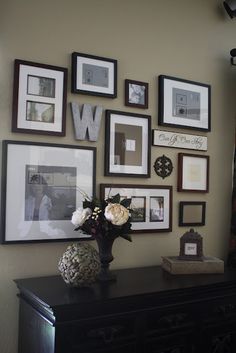 a black dresser topped with a vase filled with flowers next to pictures on the wall