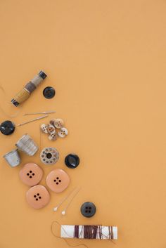 sewing supplies laid out on top of a yellow surface with thread, buttons and needles