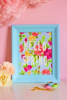 a pink flower and some scissors on a white table next to a blue frame with the words hello spring