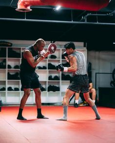 two men standing in a boxing ring, one holding a punching glove and the other wearing black shorts