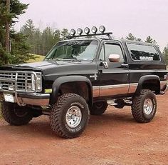 a large black truck parked on top of a dirt road in front of some trees