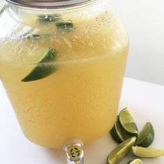 a glass jar filled with lemonade next to sliced limes