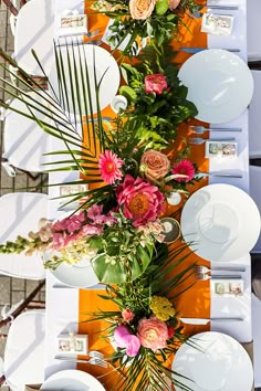 the table is set with white plates, orange napkins and colorful floral centerpieces