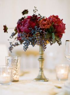 a vase filled with red flowers on top of a table next to glasses and candles