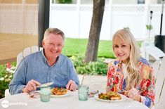 two people sitting at a table with plates of food in front of them, smiling for the camera