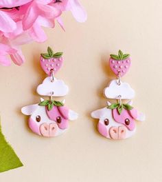 two pink and white earrings with strawberrys on top of each earring, sitting next to a pink flower