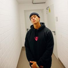 a man standing in a hallway wearing a black hoodie with a pink heart on it