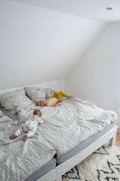 two small children laying on a bed in a room with white walls and flooring