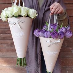 two pink cones with purple and white flowers are held by someone's hands in front of a wooden wall