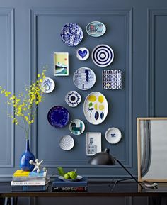 a blue wall with plates on it and a lamp next to the table in front