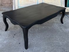 a black coffee table sitting on top of a cement floor next to a wooden door