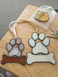 three stained glass dog paw and bone ornaments on a wooden table with a yellow ribbon