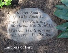 a stone with words on it sitting in the dirt next to some plants and flowers