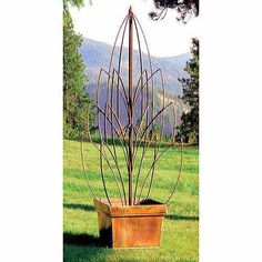 a tall metal planter sitting on top of a lush green field with mountains in the background