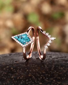 two rings with turquoise stones and diamonds on top of a rock in front of some rocks