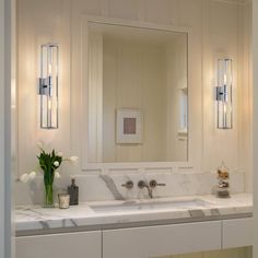 a white bathroom with marble counter tops and double sinks, along with two mirrors on the wall