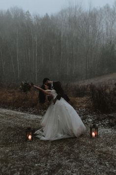 a bride and groom are kissing in the rain with candles lit up behind them on their wedding day