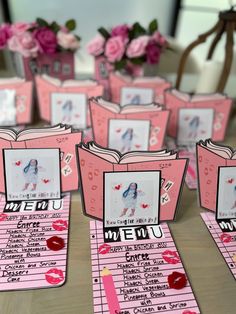 there are many small pink menus on the table with flowers in the vase behind them