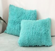 two blue pillows sitting on top of a bed next to a white headboard with a plant in the corner