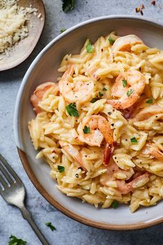 pasta with shrimp and parsley in a bowl next to silverware on a table