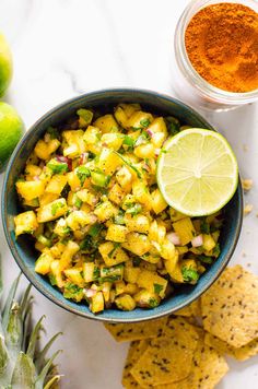 a bowl filled with pineapple salsa next to tortilla chips and lime wedges