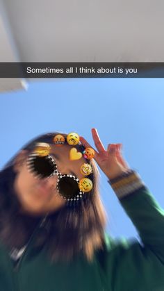 a woman with sunglasses and emoticions on her face making the peace sign while looking up into the sky