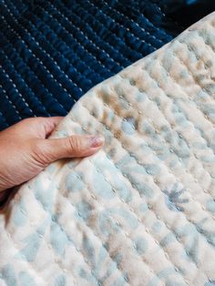 a person's hand is on top of a blue and white quilted mattress