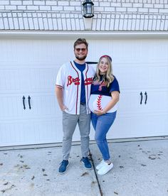 a man and woman are standing in front of a garage door with baseballs on their shirts