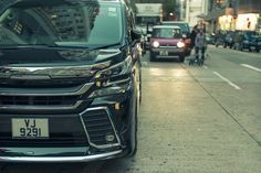 a black car parked on the side of a street next to a sidewalk with people walking down it