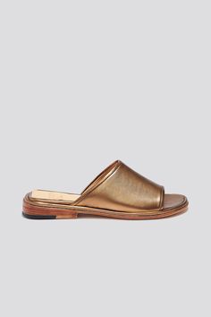 "The Pileta slide is a streamlined version of the Pileta Sport Slide, featuring a sleek leather sole. The absence of details creates the perfect canvas for metallic bronze kidskin to shine. Slipping into a simple flat sandal in a striking material can be the answer to \"\"dressing up\"\" on a summer night when paired with a long strappy dress.  Who it's for: The woman who likes being the most comfortable person at the party. Kidskin upper with vegetable tanned leather lining and a 25 mm stacked leather heel and sole.  Handmade in Argentina." Classic Gold Sandals With Leather Footbed, Gold Leather Open Toe Slides, Gold Open Toe Leather Slides, Gold Leather Footbed Slides, Gold Slip-on Slides With Leather Footbed, Gold Slides With Leather Footbed, Gold Leather Slides With Leather Footbed, Gold Leather Sandals With Rubber Sole, Sleek Gold Leather Sandals