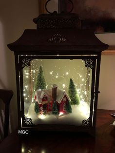 a lighted christmas scene in a glass case with trees and lights on the inside, sitting on top of a wooden table