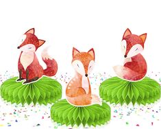 three little foxes are sitting on top of some green leafy plants and confetti