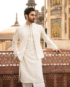 a man in a white outfit standing on a wall with his hands on his hips