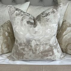 three pillows on top of a bed with white sheets and grey headboard, one is made from fabric